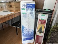 Photo of boxed 6.5 ft Lighted Winter Tree next to other boxed items and furniture.