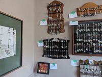 Wall-mounted wooden racks holding a variety of collector spoons with different decorative handles and emblems.