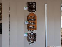 Three vertical wooden racks on a beige wall each holding about 10-15 metal collector spoons with decorated handles and tops.