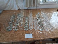 Full view of assembled set of various drinking glasses including multiple champagne flutes, water glasses, scotch tumblers, shot glasses arranged on a wood surface.