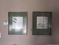 Photo of two framed Asian themed art prints hung side by side on a wall. Each has a green matte and gold frame.