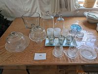 Wide shot of the assorted glass kitchen items including covered dishes, drinkware, votive holders, and a large glass bowl with spout.