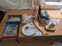 Wide view of all items on table including clock, fish plate, paddle, glass dome clock, plate hangers, and kitchen utensils.