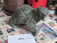 Right-side view of green-black mottled bear sculpture on newspaper with lot tag