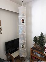 Full view of white hanging mesh organizer with plush toys inside showing five cylindrical compartments hung from ceiling.