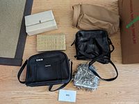 Six purses and handbags displayed on floor showing variety of styles, colors include beige, tan, black and clear with silver spikes.