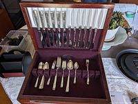 Opened wooden case displaying the upper section with knives and forks in slots, partially showing spoons in the lower compartment.