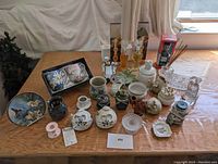 Overview image showing a collection of various small ceramic household items including mugs, candle holders, canisters, decorative plates, and figurines arranged on a table.