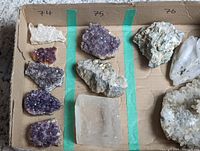 Three crystals arranged on cardboard sections marked 74, 75, 76: white/clear quartz, purple amethyst cluster, and large optical calcite.