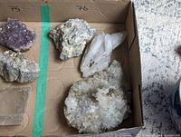 Wide shot of three crystals in a cardboard box showing a quartz cluster, quartz spar, and a blue kyanite-like crystal.