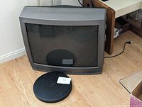 Front view of Toshiba CRT TV beside the round black swivel stand base on a wooden floor.
