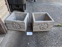 Two concrete square planters placed outdoors, showing front and side raised decorative circular symbols.