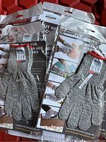 Lot display of multiple pairs of grey cut resistant gloves in plastic packaging with a red plastic board behind.