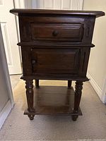 Front view of one wooden side table showing drawer, cabinet door, lower shelf, and turned legs.