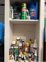 Photo of white shelving unit containing various household cleaning supplies including Downy Fresh fabric softener, Comet powder cleaner, carpet cleaner, spray bottles of cleaning liquids, lamp oil, and other assorted bottles of cleaners and chemicals.