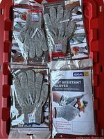 Photo showing multiple pairs of grey knitted cut resistant gloves in packaging on a red plastic board background.