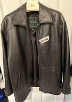 Front view of the Danier men's black leather jacket hanging on a hanger, showing the collar, zip front, and side pockets.
