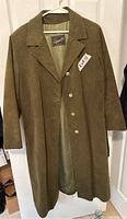 Brown men's long leather coat hanging on hanger showing front with button closure and lapel collar.