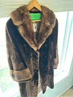 Full view of men's brown fur coat hanging on wooden hanger shows plush full fur collar and soft fur cuffs.