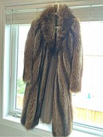 Full view of men's XL brown fur coat hanging by window showing length and fur texture
