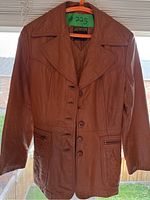 Front full view of brown leather jacket with button front closure, two zippered pockets, and quilted detailing.
