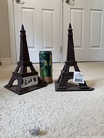 Pair of metal Eiffel Tower shaped book ends standing upright on carpet beside a 330 ml Perrier can for scale.