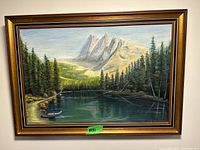 Framed landscape painting showing lake with small boat docked, pine trees and mountain range in background.