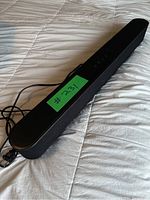 Photo of black sound bar lying on bed showing fabric front cover and attached cord