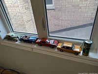 Four metal toy cars arranged on a windowsill with a 330ml Perrier can for size reference.