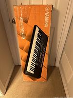 Yamaha PSR-E263 keyboard in its original orange box, positioned vertically.