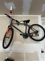 Full side view of the gray and orange Powell mountain bike hanging on a wall mount, showing the frame, tires, pedals, and handlebars.