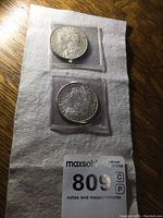 Both 1901 and 1902 silver dollar coins in protective holders on a white cloth background.