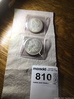 Photo showing both 1921 and 1904 Morgan silver dollars in separate plastic holders placed on white cloth.