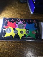 Set of six Canadian coins mounted in plastic sleeve with colorful maple leaf background and CANADA printed in red.