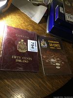 Two vintage coin books: Canada Fifty Cents 1946-1963 in maroon and Canada 50 Cents 1964-1987 in brown, side by side on a wooden surface.