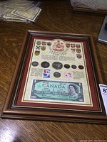 Full view of the framed 1967 Canadian Centennial Collection showing coins, stamps and paper bill inside a 9x12 brown wooden frame with red matte.
