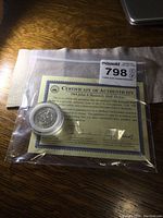Photo of the JFK half dollar coin in hard plastic case alongside the Certificate of Authenticity.