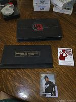 Lot contents arranged on wooden table: black box with red 23 logo, Farewell box, white commemorative stamp box with Michael Jordan silhouette, baseball card in plastic sleeve