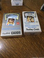 Two closed boxes of North Carolina Tar Heels trading cards, one First Edition and one Second Edition, sitting on a wooden table.