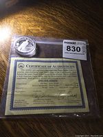 Photo showing the coin and certificate of authenticity in a clear plastic bag on a wooden surface.