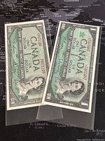 Two Canadian one dollar banknotes (1954 and 1967) in protective sleeves showing front side with Queen Elizabeth II portrait.