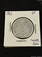 Reverse of the 1961 Canadian 50 cent silver coin featuring the Canadian coat of arms, date, and silver content marking in EF condition holder.