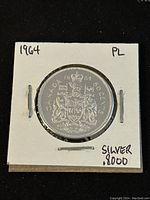 Front (reverse) of the 1964 Canadian 50 cent silver coin showing the Coat of Arms with the year 1964 and 'Canada 50 Cents' inscription, encased in a cardboard holder.