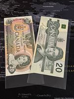 Two Canadian $20 banknotes from 1979 and 1991 displayed overlapped on a world map background.