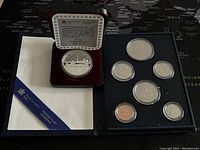 Overall view of the 7 coin set including the box and protective cases showing all coins and certificate
