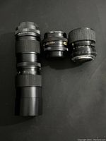 Three assorted camera lenses laid flat on black surface