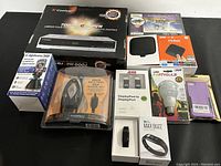 Nine assorted electronic items on a black surface, shown from above including each item's original packaging and product.