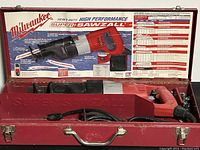Opened red metal carrying case showing Milwaukee Super Sawzall inside with power cord and interior label with detailed information and charts