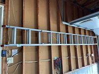 Side view of full 24-foot aluminum extension ladder hung horizontally on wooden garage wall.