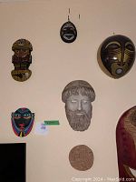 Six international masks varying in size and style hanging on a light-colored wall, showing African-style, classical, and abstract designs